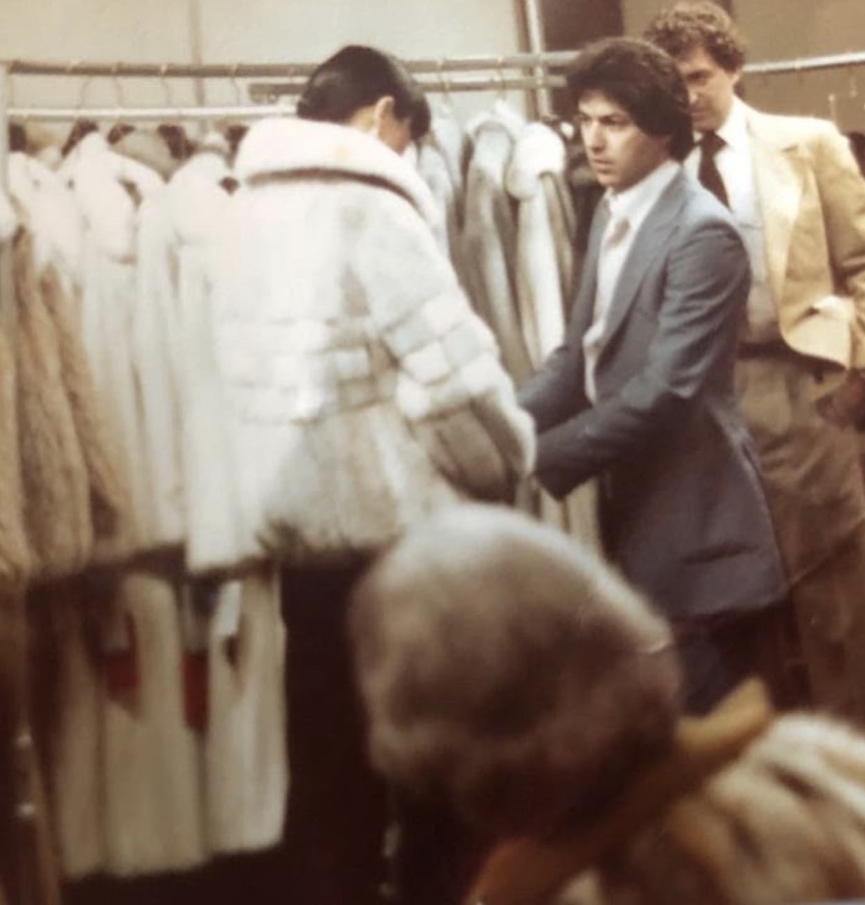Ervin Rosenfeld, a young furrier in a blue suit, assisting a customer among racks of fur coats in the ERNY Furs showroom in Manhattan's Fur District.